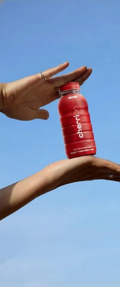 A hand balancing a red CherriOn bottle against a blue sky
